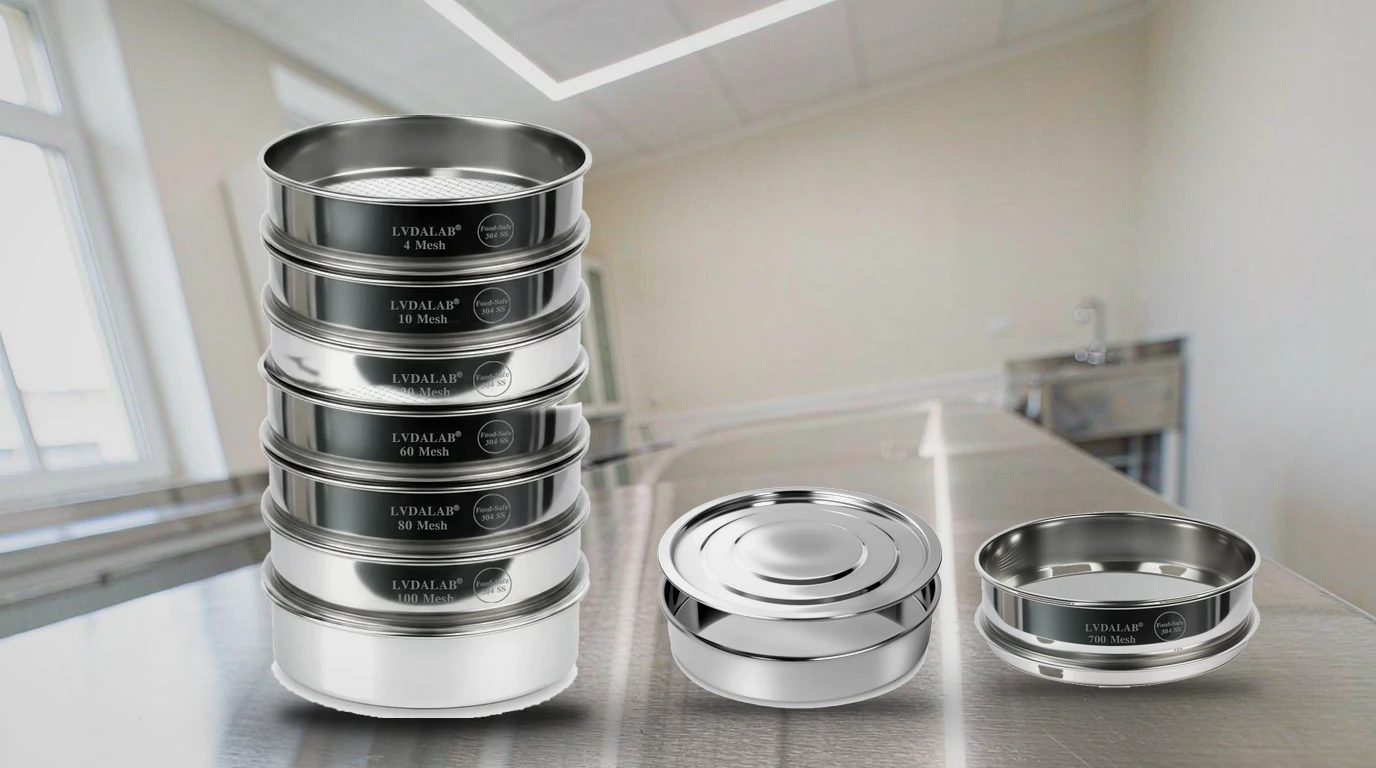 A stacked set of LVDALAB 304 stainless steel test sieves with a collection pan and lid, beside a loose 200 mm sieve, arranged on a stainless steel laboratory bench